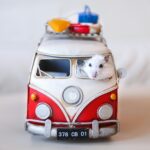 A tiny white mouse peeking out of a toy Volkswagen van with travel gear, creating a playful scene.
