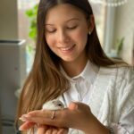 A young woman smiling while gently holding a cute pet hamster indoors.